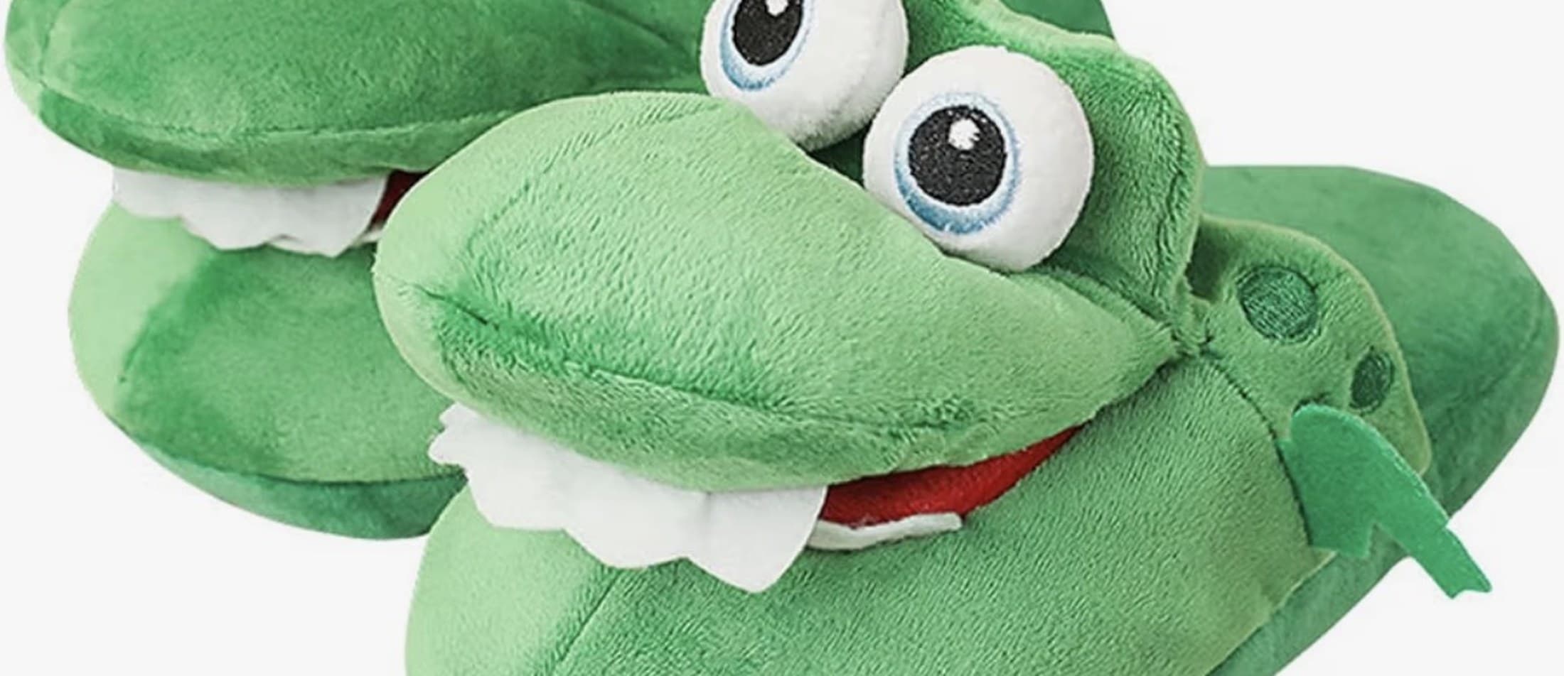 Deux chaussons crocodile en peluche verte vus de près, gros yeux ronds, dents blanches et langue rouge.