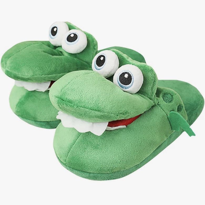 Une paire de chaussons crocodile en peluche verte, gros yeux ronds et dents blanches.