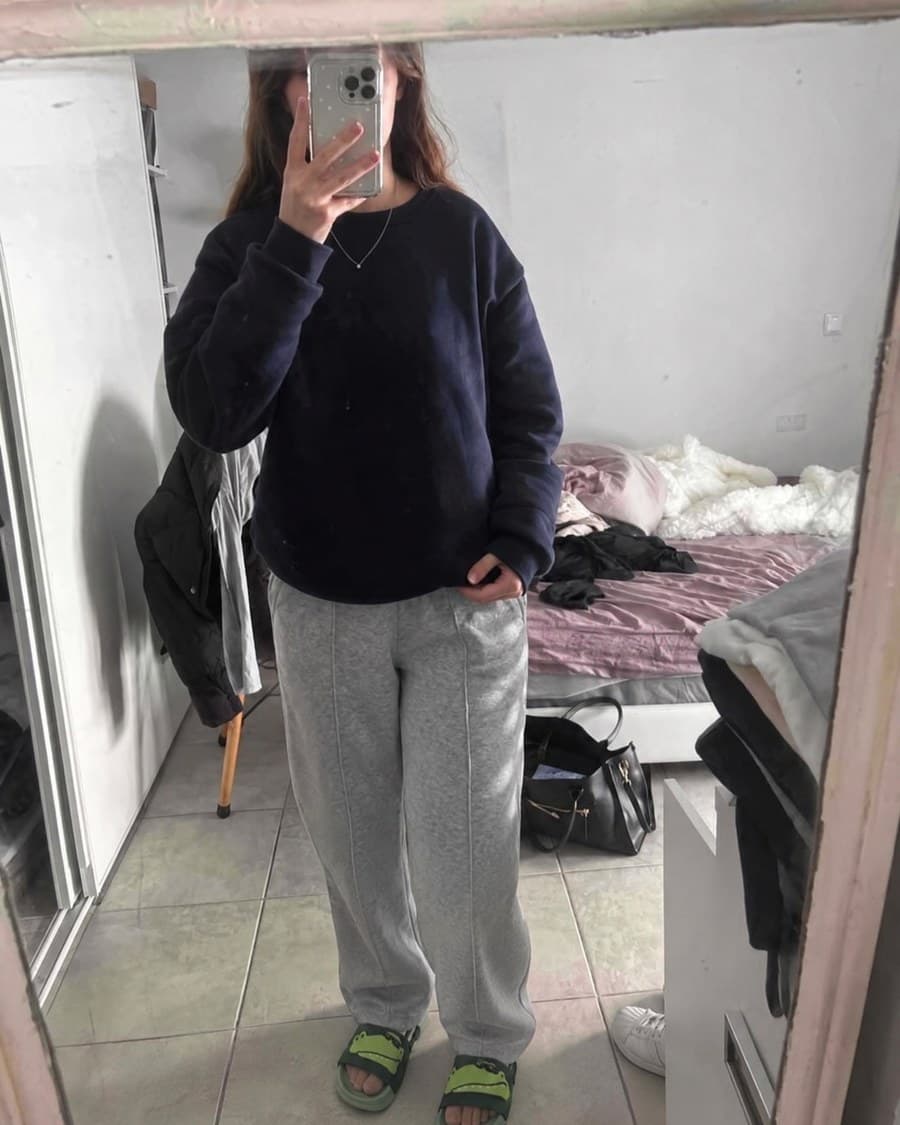 Les claquettes crocodile portées avec un jogging gris, photographiées dans un miroir de chambre.