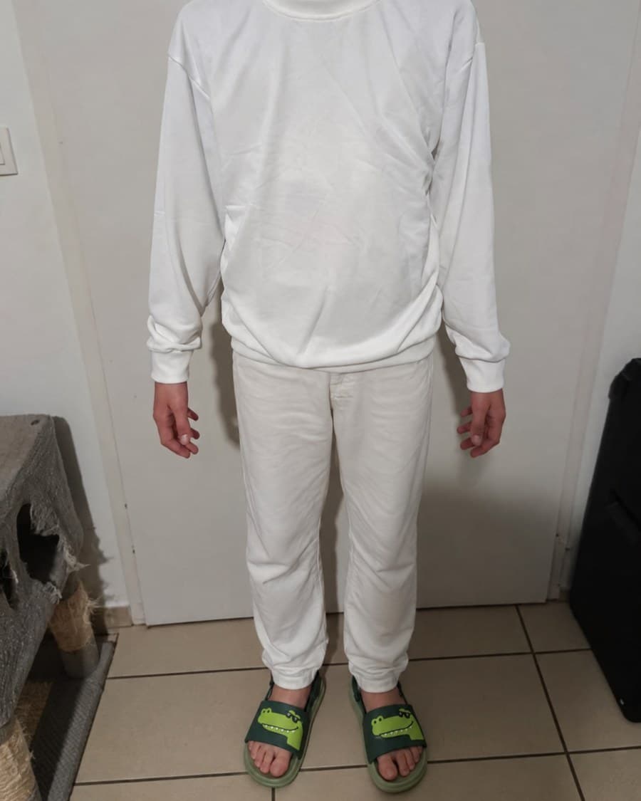 Les claquettes crocodile portées avec un ensemble blanc, vues de face sur un carrelage clair.