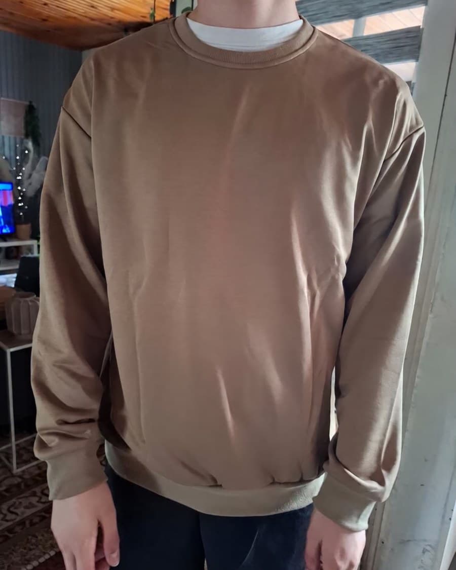 Un client en sweat camel, photographié de face, cadré au-dessus des pieds.