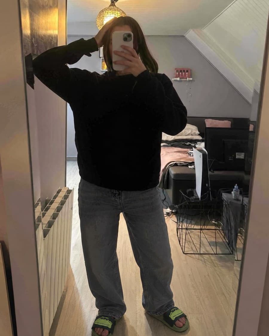 Les claquettes crocodile portées avec un jean large, photographiées dans un miroir.