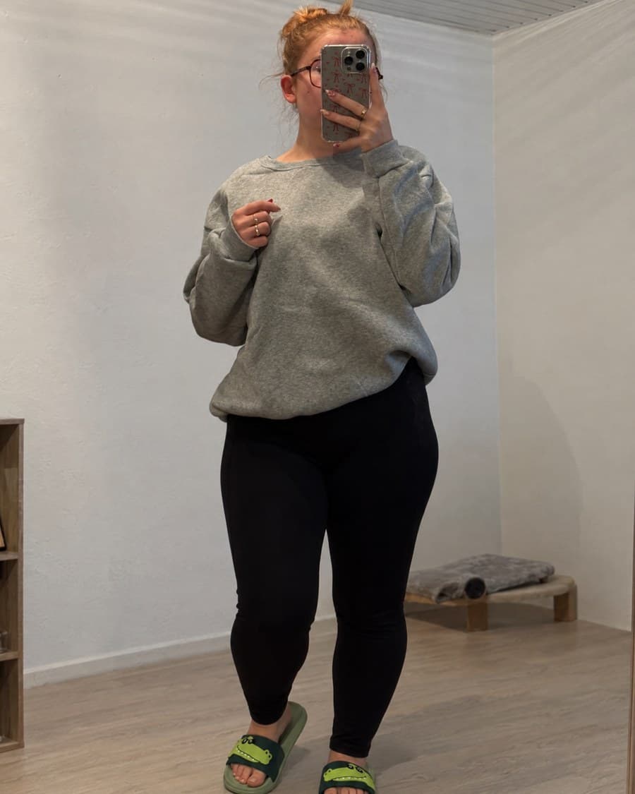 Les claquettes crocodile portées avec un sweat gris et un legging noir, photographiées dans un miroir.